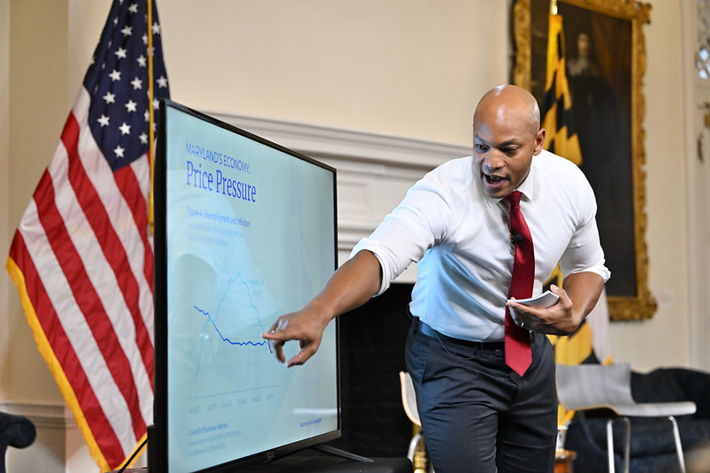 Governor Moore speaks while pointing to content displayed on a television screen.
